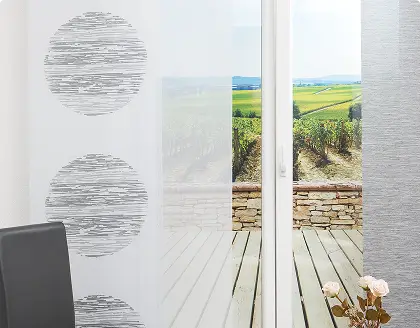 Eine bedruckte Schiebegardine mit grauen Kreisen kombiniert mit passenden unifarbenen Flächenvorhängen hängt vor einer Terrassentür