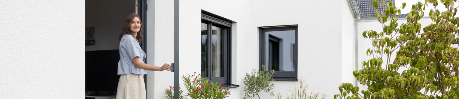 Frau öffnet eine moderne Fliegengitter Tür an einem weißen Haus mit anthrazitfarbenen Fenstern