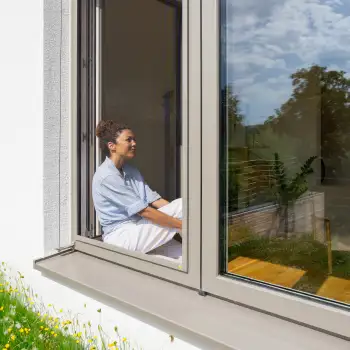 Frau sitzt entspannt im offenen Fenster mit eingesetztem Fliegengitter Spannrahmen SP 1/5